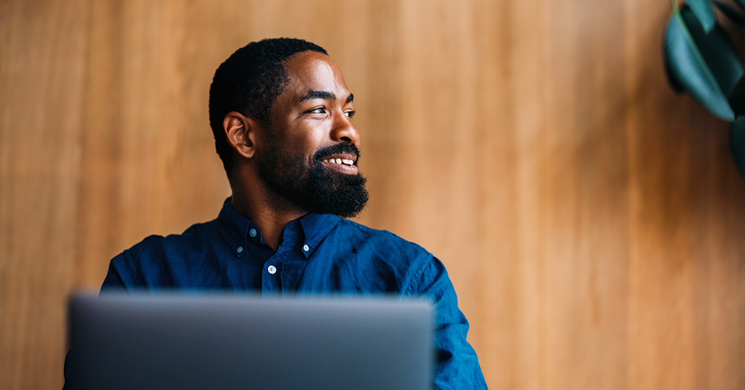 A man working on his laptop with a wood wall behind him