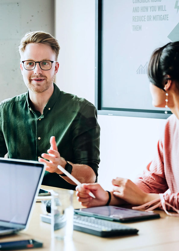 A man with glasses and a green shirt gestures while talking to a woman about Blackboard LMS