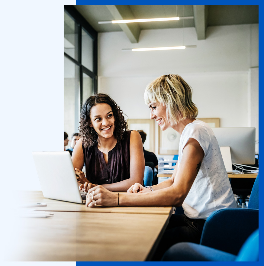 Photo of two women seated at a table collaborating at a laptop